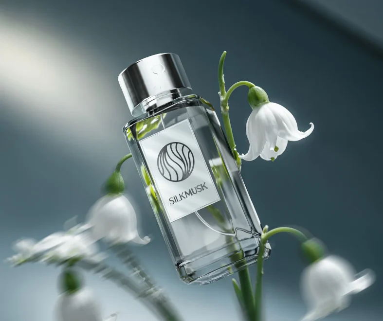 A clear SilkMusk perfume bottle with silver cap rests among white bell-shaped flowers, softly lit against a dark blue background, serene.