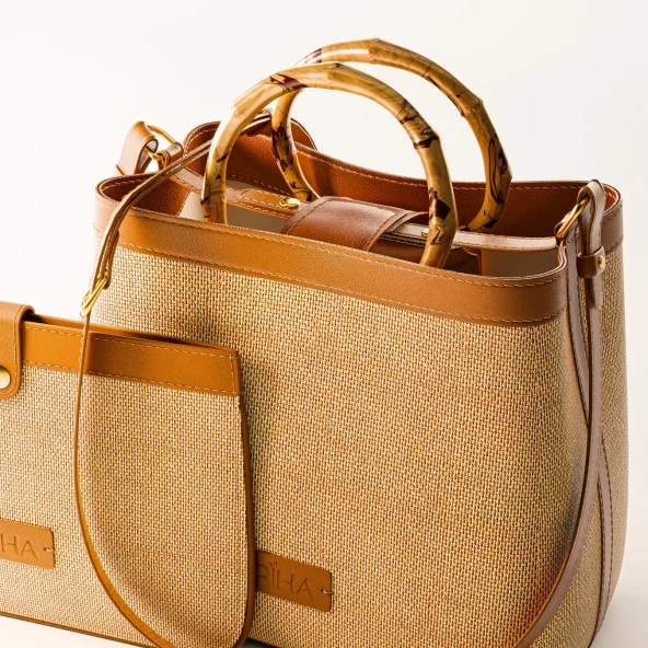 Woven straw handbag with tan leather trim, bamboo handles, front pocket, and side strap; warm, stylish design on a neutral background.