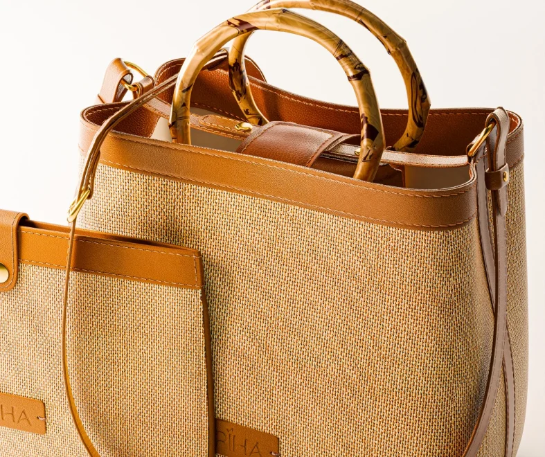 Woven straw handbag with tan leather trim, bamboo handles, front pocket, and side strap; warm, stylish design on a neutral background.