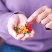 A pair of hands holds colorful gummy candies, with a purple shirt in the background.