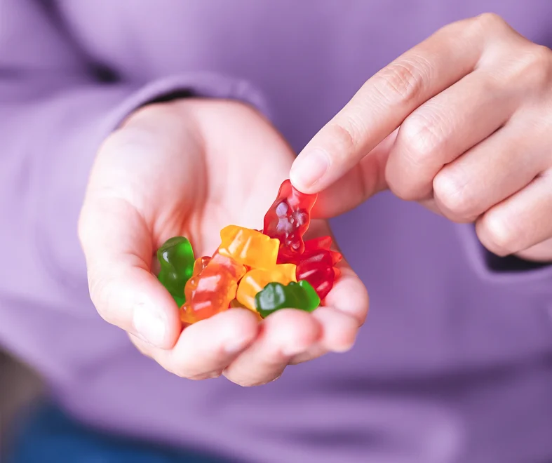 A pair of hands holds colorful gummy candies, with a purple shirt in the background.