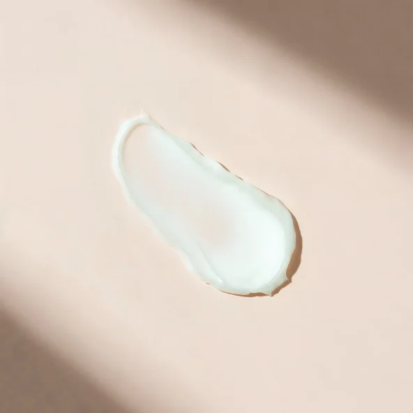 A dollop of white cream or lotion on a beige surface with soft shadows.