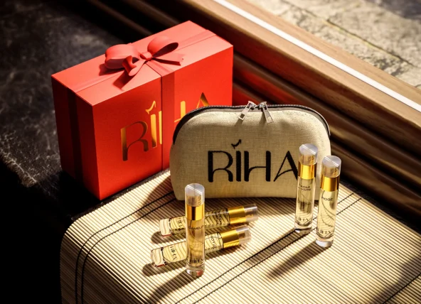 Luxury Riha perfume gift set with a red ribboned box, beige branded pouch, and gold fragrance bottles arranged on a sunlit table.