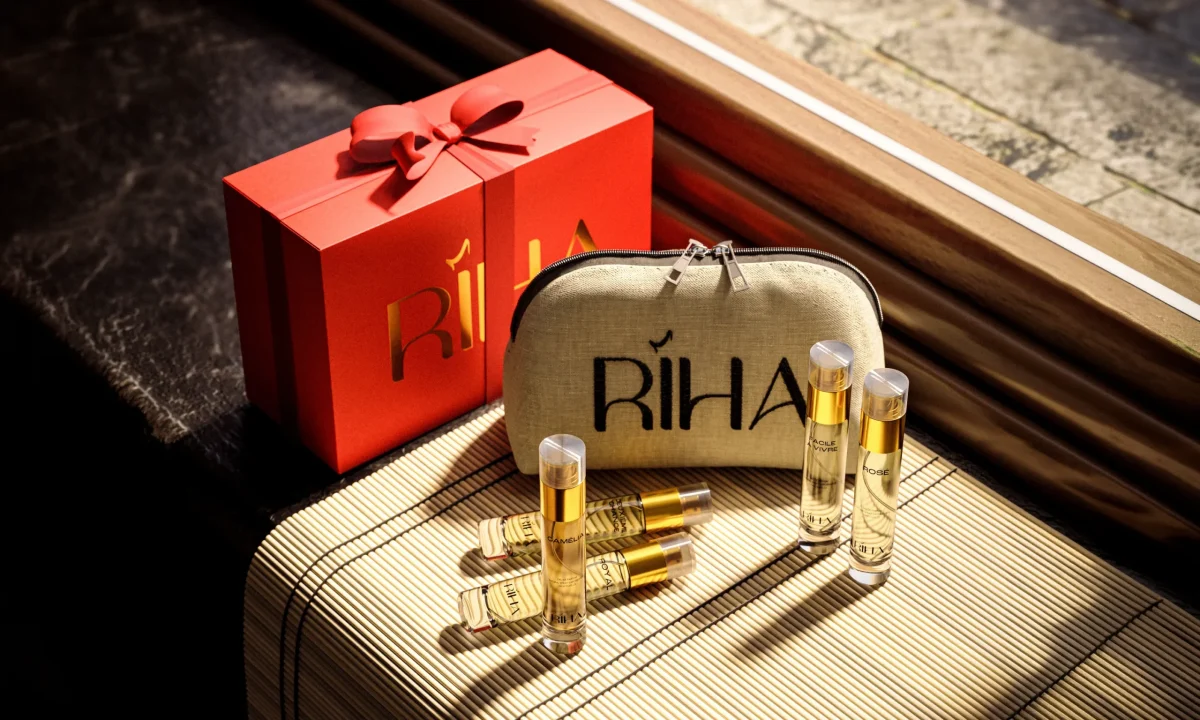 Luxury Riha perfume gift set with a red ribboned box, beige branded pouch, and gold fragrance bottles arranged on a sunlit table.